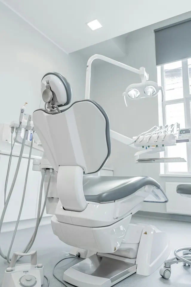 A treatment room with a white dental chair beside a large window